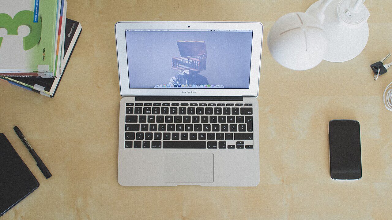 Laptop computer open on a wooden desk beside books and a phone